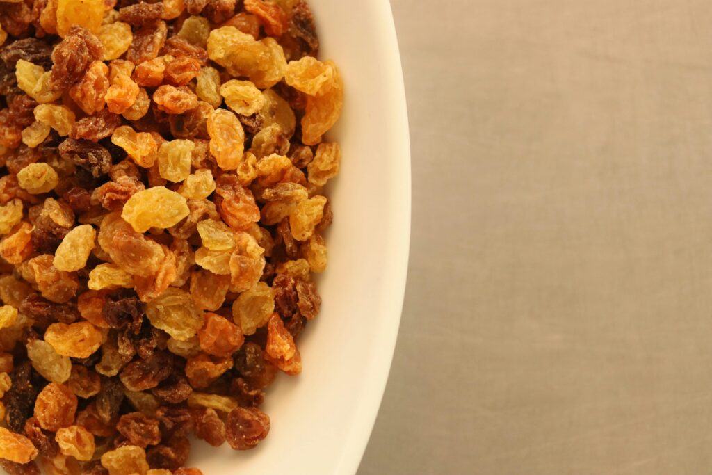 Close-up of assorted yellow and brown raisins in a white bowl on a textured background.